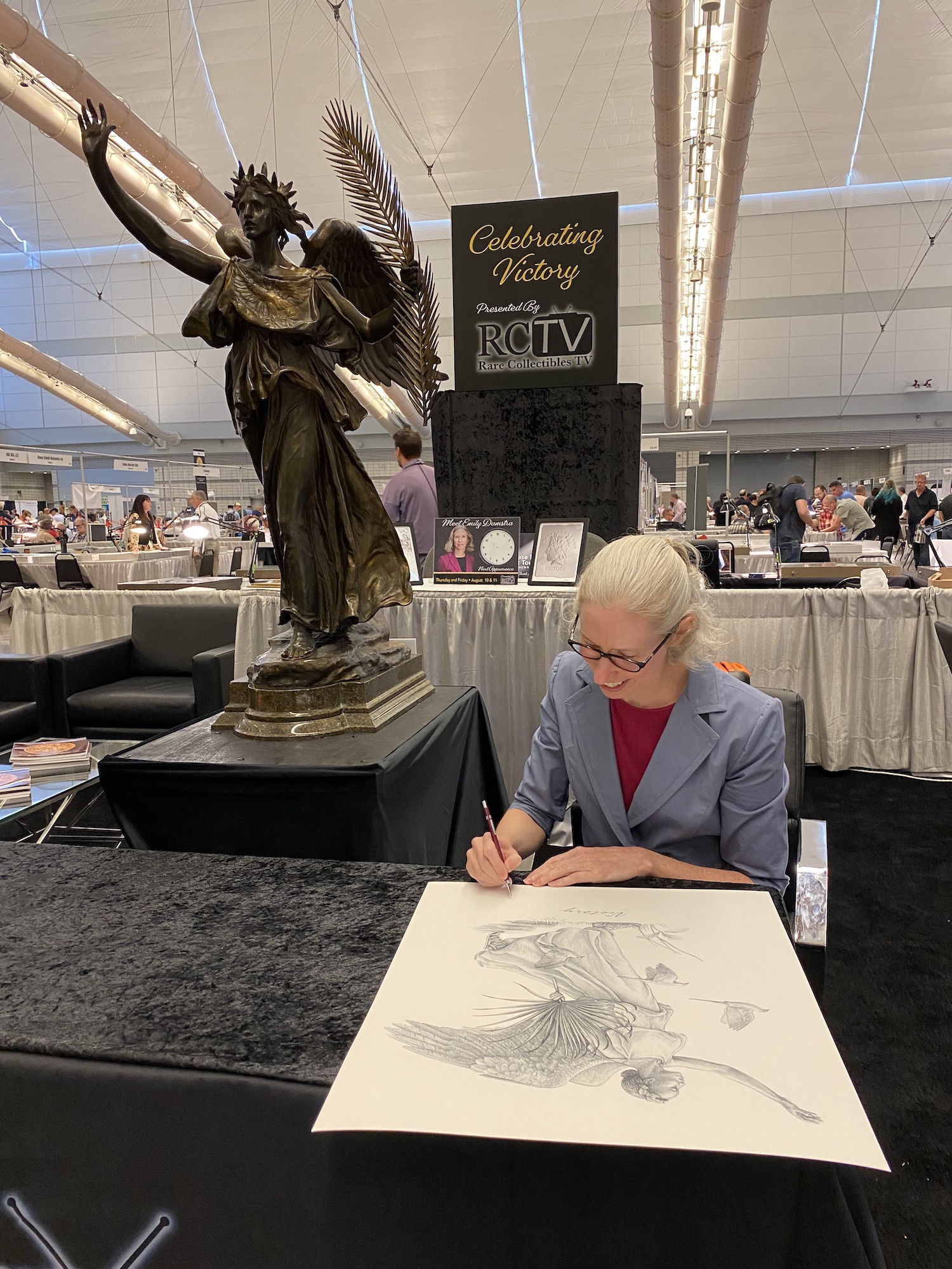 Photo of Emily signing large print in front of Victory sculpture